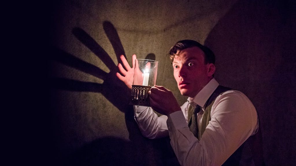 From The Woman in Black, a man holding his hand up to a lantern, creating a large shadow on the wall behind him