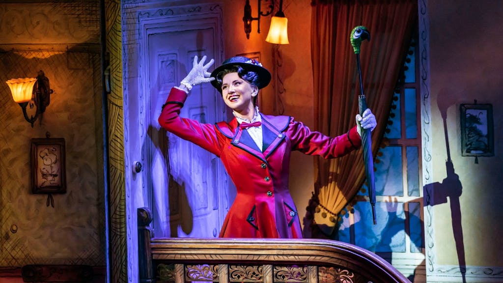Mary Poppins holding her hat, dressed in a red coat with her umbrella